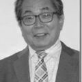 안경을 쓰고, 정장을 입고, 무늬가 있는 넥타이를 매고, 카메라를 향해 웃고 있는 남성의 흑백 초상화.