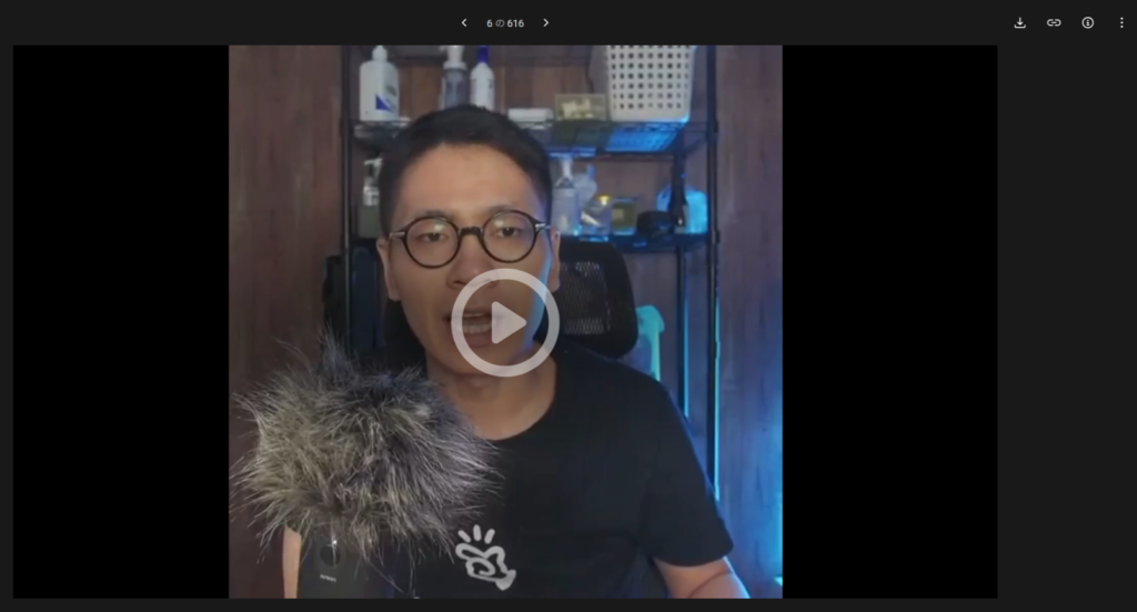 【2026年】pCloudバレンタインセールはいつ?2月限定の買い切り割引キャンペーンが発表!お得? 眼鏡をかけ、黒いシャツを着た人物が、毛皮のついたウィンドスクリーンのついたマイクの前に座り、ボトルやバスケットの棚を背景に、pCloudに関するコンテンツを録音している。.